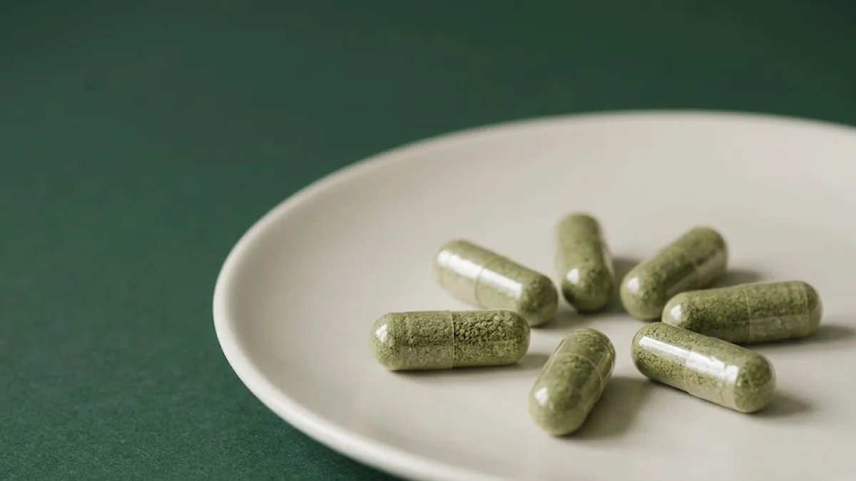 Green kratom capsules resting on a plain ceramic plate.
